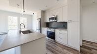 Located at 521 Broad St in Halifax, NS, this thoughtfully designed 4-bedroom, 2-bathroom unit offers a generous, well-appointed single-floor layout. The open-concept kitchen and living area serves as the heart of the home, showcasing wide-plank hardwood-style flooring, crisp white walls, and abundant natural light streaming through multiple windows. The modern kitchen is equipped with full-height white cabinetry, a sleek tile backsplash, stainless steel appliances including a range, microwave, and refrigerator, and a central island with an undermount sink — ideal for both cooking and casual dining. The living room features direct access to a private balcony with glass-panel railings and a wood-ceiling overhang, overlooking a natural, treed landscape. Each of the four bedrooms offers clean lines and durable flooring, with the spacious primary bedroom complemented by a large walk-in closet with built-in shelving and hanging rods. The two bathrooms are finished with neutral tile work, including a full tub-shower combination. A dedicated in-unit laundry room houses a stacked Samsung washer and dryer. Two hallways and three closets provide ample additional storage throughout this well-organized, modern home.