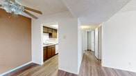 Located at 10330 Gateway Blvd N in El Paso, Texas, this one-bedroom, one-bathroom unit offers a practical and efficient layout across a single floor. The interior features wood-look flooring throughout the main living and kitchen areas, creating a warm and cohesive aesthetic complemented by clean white walls and a textured ceiling.

The kitchen is thoughtfully appointed with rich, dark wood cabinetry providing ample upper and lower storage, a white countertop with an integrated sink, and a full-size refrigerator. A skylight-style window above the cabinetry brings in additional natural light, enhancing the brightness of the space.

A central hallway connects the main living area to the private quarters, offering a clear and organized flow through the unit. The bedroom is comfortably sized, featuring plush carpet flooring, a window with blinds for natural light and privacy, and direct access to a dedicated walk-in closet. The closet is equipped with a built-in shelving unit and hanging rods, maximizing storage capacity.

The bathroom is finished with full white tile surrounding a soaking bathtub and shower combination, maintaining a clean and classic look. A ceiling fan in the living area and ample wall outlets throughout round out the functional details of this efficiently designed unit.
