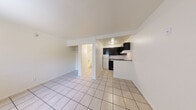 Located at 110 S Bruce St, Unit 114, in Las Vegas, NV, this studio unit offers a practical and efficient single-floor layout. Light-colored ceramic tile flooring runs throughout the entire space, lending a clean, cohesive look. The open main living area features neutral white walls, a wall-mounted HVAC unit, and a window fitted with vertical blinds that allows natural light to filter in. An open closet with a built-in rod provides convenient storage directly within the living space. The kitchen is positioned in a defined nook and features dark cabinetry with a bold contrast against granite-style laminate countertops. A white electric coil range with a ventilation hood, an under-counter appliance space, and a compact sink complete the kitchen's functional layout. The bathroom includes light-toned tile flooring consistent with the rest of the unit, a full soaking tub with a shower and curtain rod, a toilet, a white vanity with a mirrored medicine cabinet above, and a wall-mounted light bar. The textured walls throughout add subtle depth to the overall aesthetic. This unit offers a straightforward, no-frills design well-suited for efficient everyday living in a central Las Vegas location.