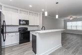Located at 27011F Seabiscuit Ln in Greensboro, NC, this well-appointed single-floor residence offers a clean, modern aesthetic with consistent finishes throughout. The open-concept kitchen serves as the heart of the home, showcasing white shaker cabinetry that extends to the ceiling, a classic subway tile backsplash, black appliances including a refrigerator, range, and microwave, and a striking navy blue island topped with light marble-style countertops. Pendant lighting adds a refined touch above the island, which also features an undermount sink. Wood-look luxury vinyl flooring flows seamlessly through the main living areas, enhancing the bright, airy feel of the space. The bedrooms are finished with plush carpeting and feature natural light through slatted blinds, with ceiling fans providing additional comfort. A spacious walk-in closet with wire shelving and hanging rods offers generous storage. The bathroom is thoughtfully designed with white cabinetry, dark granite countertops, brushed nickel fixtures, a large vanity mirror, and a glass-enclosed shower. Clean white walls and crisp baseboards throughout lend a fresh, move-in-ready appeal to this inviting Greensboro residence.