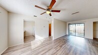 Located at 5565 Connie Jean Rd in Jacksonville, FL, this single-story home offers four bedrooms and one bathroom within a compact, efficiently designed floor plan. Light-toned wood-look flooring runs throughout the home, creating a cohesive and easy-to-maintain interior. The open living room features a ceiling fan and a sliding glass door that fills the space with natural light and provides direct access to the outdoor area. A textured ceiling adds a classic touch to the living space. The kitchen is laid out in a practical galley style, featuring wooden cabinetry, light stone-look countertops, a stainless steel sink with a window above it, and white appliances including a range and refrigerator. Louvered closet doors and an adjacent open storage area provide added utility. Each of the four bedrooms is finished with the same wood-look flooring and includes closet space with wire shelving. The primary bedroom features a large sliding glass door offering outdoor views and additional natural light. The single full bathroom is cleanly appointed with a vanity, mirror, and a tub-shower combination unit.