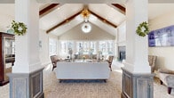 Located at 10217 Cherry Ln in Nampa, Idaho, this beautifully appointed single-story clubhouse showcases a sophisticated blend of architectural character and modern comfort. The grand main living area commands attention with soaring vaulted ceilings accented by rich exposed wood beams, a striking circular transom window, and a statement sputnik chandelier in gold. Banks of large windows flood the space with natural light and offer views of the outdoor pool and surrounding community. Decorative columns with detailed millwork frame the transition between the entryway and the main lounge, which is anchored by a tile-surround fireplace with shiplap accent wall and a mounted television. A dedicated billiards room features light hardwood floors, generous window placement, and an industrial-style geometric pendant light above the pool table. The well-equipped kitchen is outfitted with grey shaker cabinetry, granite countertops, a mosaic tile backsplash, stainless steel appliances, and light hardwood flooring. Additional seating areas throughout the space feature neutral-toned furnishings, carpeted floors, and abundant natural light, with direct access to the outdoor patio and pool area, creating a seamless indoor-outdoor connection ideal for community gatherings.