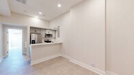 Located at 305 W Fourth St in downtown Winston-Salem, NC, this 2-bedroom, 1-bathroom unit offers a well-designed layout that maximizes its compact footprint. The open living area flows seamlessly into the kitchen, which features a peninsula counter with a pass-through design, gray shaker-style cabinetry with matte black hardware, white quartz countertops, a subway tile backsplash, and a full suite of stainless steel appliances including a French door refrigerator, electric range, and over-the-range microwave. Recessed lighting throughout keeps the space bright and modern. A hallway connects the living area to the two bedrooms and bathroom, maintaining a clear and functional layout. The primary bedroom is a well-proportioned room with large black-framed windows that bring in abundant natural light and views of the surrounding area. The second bedroom similarly benefits from natural light through its own windows. The bathroom features a walk-in shower with white subway tile surround and a frameless glass door with brushed nickel hardware. Soft, neutral carpeting runs throughout the bedrooms and living areas, complementing the clean white walls and bold white baseboards that give the entire unit a crisp, contemporary aesthetic.