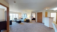 This single-floor residence offers a thoughtfully laid-out living space with a comfortable, functional design throughout. The expansive living room is carpeted and bathed in natural light through large windows that frame outdoor views, creating a bright and welcoming atmosphere. The room provides ample space for multiple seating arrangements and includes dedicated areas for both relaxing and entertainment.

The galley-style kitchen is well-equipped with warm honey-toned wood cabinetry, laminate countertops, stainless steel appliances including a refrigerator, electric range, and dishwasher, and wood-look flooring that extends through the dining area. The kitchen opens toward a dining space with a ceiling fan overhead.

The residence includes multiple bedrooms, each carpeted and accented with neutral walls. The bedrooms feature generous closet storage, ceiling fans or ambient lighting, and windows that allow natural light to fill the rooms. Coordinating framed artwork adds a polished touch to each space.

The bathroom is finished with rich wood-look flooring, an extended vanity with warm wood cabinetry and a wide mirror, and a separate shower area. Throughout the home, warm wood door and trim accents provide a cohesive, inviting aesthetic that ties each room together seamlessly.