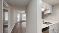 Located at 740 Sidney Marcus Blvd NE in Atlanta's 30324 zip code, this single-floor residence offers a thoughtfully designed layout with a clean, contemporary aesthetic throughout. Rich, dark hardwood-style flooring extends across the main living areas, complementing the neutral warm-gray wall tones that create a bright and welcoming atmosphere.

The open living area is generously proportioned, bathed in natural light streaming through multiple windows fitted with horizontal blinds. A ceiling fan serves as a central fixture, enhancing comfort throughout. The space flows seamlessly toward the entry and connects to the adjacent kitchen via a half-wall passthrough, providing an open and connected feel.

The kitchen is well-appointed with white shaker cabinetry, light countertops, a stainless steel sink, a dishwasher, and a full suite of stainless appliances including a refrigerator, electric range, and over-the-range microwave. The galley-style configuration maximizes storage and functionality.

The bedroom is spacious and well-lit, featuring a ceiling fan, a closet, and direct access to a bathroom with white cabinetry and vanity. A private balcony off the unit offers pleasant views of mature trees, providing a peaceful outdoor retreat within an urban setting.