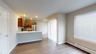This single-floor residence offers a clean, modern layout designed for comfortable everyday living. The open-concept kitchen and living area serves as the heart of the home, featuring warm wood-toned cabinetry, a full suite of stainless steel appliances including a refrigerator, range, microwave, and dishwasher, and a light-colored countertop island with an integrated sink. A tile backsplash adds a polished touch to the kitchen, while durable wood-look flooring extends throughout the main living spaces, providing a cohesive and easy-to-maintain aesthetic. Large sliding glass doors and windows allow natural light to fill the open living and dining area, creating a bright and welcoming atmosphere. The bedrooms are carpeted for comfort and feature neutral wall tones, recessed lighting, and ample closet space, with at least one room including a dedicated reach-in closet. The bathroom is well-equipped with a combined tub and shower, a single-sink vanity with wood cabinetry, a white countertop, and a mirror with overhead lighting. Baseboard heating units are present in key rooms, and recessed lighting throughout ensures consistent illumination. The overall design is practical and clean, with a neutral color palette that creates a calm and versatile living environment.