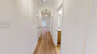 This single-story home delivers a clean, modern aesthetic through a cohesive palette of crisp white walls and warm-toned luxury vinyl plank flooring that extends throughout every room. The hallways are brightened by stylish pendant lighting and black hardware accents on paneled doors, creating an inviting path through the home. The open kitchen and living area serves as the heart of the space, featuring warm wood cabinetry, speckled granite countertops, stainless steel appliances including a range, refrigerator, and microwave, along with a central island with a sleek black faucet and single-basin sink. The living area connects to the outdoors through a glass door and window, allowing natural light to fill the space. The three bedrooms are comfortably sized, with the primary bedroom offering its own dedicated closet. Secondary bedrooms feature ceiling fans and windows with views of the surrounding greenery. Both bathrooms are finished with matching wood vanities, granite countertops, undermount sinks, and black fixtures. The primary bath includes a tub-shower surround with clean tile work. A dedicated laundry room houses a full-size washer and dryer beneath overhead cabinetry, adding practical convenience. An attached garage completes this thoughtfully designed home.