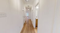 This single-story home delivers a clean, modern aesthetic through a cohesive palette of crisp white walls and warm-toned luxury vinyl plank flooring that extends throughout every room. The hallways are brightened by stylish pendant lighting and black hardware accents on paneled doors, creating an inviting path through the home. The open kitchen and living area serves as the heart of the space, featuring warm wood cabinetry, speckled granite countertops, stainless steel appliances including a range, refrigerator, and microwave, along with a central island with a sleek black faucet and single-basin sink. The living area connects to the outdoors through a glass door and window, allowing natural light to fill the space. The three bedrooms are comfortably sized, with the primary bedroom offering its own dedicated closet. Secondary bedrooms feature ceiling fans and windows with views of the surrounding greenery. Both bathrooms are finished with matching wood vanities, granite countertops, undermount sinks, and black fixtures. The primary bath includes a tub-shower surround with clean tile work. A dedicated laundry room houses a full-size washer and dryer beneath overhead cabinetry, adding practical convenience. An attached garage completes this thoughtfully designed home.