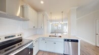 This three-story home is thoughtfully designed with a clean, modern aesthetic and functional layout across all levels. A central staircase with warm wood treads, white risers, and a classic turned newel post serves as the spine of the home, connecting each floor with an open view to the living areas below.

The kitchen is a standout feature, outfitted with white shaker-style cabinetry accented by matte black hardware, bright white quartz countertops, and a classic subway tile backsplash. Stainless steel appliances include an electric range with a sleek wall-mounted hood vent, a side-by-side refrigerator, and a dishwasher. A peninsula with an undermount sink opens directly to the dining and living areas, which are brightened by natural light from multiple windows and a sliding glass door leading to an outdoor balcony. Ceiling fans are present in the living areas, enhancing comfort throughout.

The bathroom features a full tub-shower combo with a clean white surround, a white vanity with an undermount sink, and tile flooring. Neutral tones and consistent hardwood-style flooring run throughout, creating a cohesive and inviting atmosphere across all three floors.