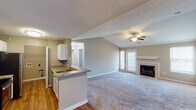 This single-floor residence offers a thoughtfully designed layout that balances comfort and functionality throughout. The open-concept living area is a standout feature, showcasing soaring vaulted ceilings accented by a ceiling fan, plush carpeting, and a tile-surround fireplace with a classic white mantel. A sliding glass door fills the space with natural light and provides access to the outdoors. The kitchen is equipped with stainless steel appliances — including a range, over-the-range microwave, and refrigerator — complemented by granite-look countertops, white cabinetry, and hardwood flooring. A peninsula with a sink connects the kitchen to the main living area. A separate dining or flex space features hardwood floors, recessed lighting, and elegant crown molding. The bedrooms are carpeted and generously sized; the primary bedroom impresses with its own vaulted ceiling and direct access to an en suite bathroom. The bathrooms are well-appointed, featuring a soaking tub and shower combo, granite-look vanity countertops, and ample storage. Neutral warm-gray tones carry throughout, creating a cohesive and inviting atmosphere from room to room.