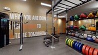 Located at 2625 N Clark St in Chicago's Lincoln Park neighborhood, this single-floor fitness facility is designed to inspire and energize its users through bold, purposeful design. The space is divided into distinct zones, each tailored to a specific type of training.

The main gym area features soaring ceilings with exposed ductwork and industrial-style linear lighting, creating an open, high-energy atmosphere. Large motivational phrases are emblazoned across textured accent walls in orange, white, and gray, reinforcing the facility's energetic brand identity. This area is equipped with treadmills, ellipticals, power racks, barbells, weight plates, kettlebells, medicine balls, and cable machines, providing a comprehensive range of strength and cardio options. Durable rubber flooring throughout ensures safety and functionality.

A separate studio room offers a clean, minimalist contrast to the main floor. Bright white walls, light flooring, full-length mirrors, and softer lighting create a calm environment suited for yoga, stretching, and functional movement. The studio is stocked with exercise mats, stability balls, and BOSU trainers. Together, the two zones deliver a well-rounded, professional fitness environment.