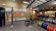 Located at 2625 N Clark St in Chicago's Lincoln Park neighborhood, this single-floor fitness facility is designed to inspire and energize its users through bold, purposeful design. The space is divided into distinct zones, each tailored to a specific type of training.

The main gym area features soaring ceilings with exposed ductwork and industrial-style linear lighting, creating an open, high-energy atmosphere. Large motivational phrases are emblazoned across textured accent walls in orange, white, and gray, reinforcing the facility's energetic brand identity. This area is equipped with treadmills, ellipticals, power racks, barbells, weight plates, kettlebells, medicine balls, and cable machines, providing a comprehensive range of strength and cardio options. Durable rubber flooring throughout ensures safety and functionality.

A separate studio room offers a clean, minimalist contrast to the main floor. Bright white walls, light flooring, full-length mirrors, and softer lighting create a calm environment suited for yoga, stretching, and functional movement. The studio is stocked with exercise mats, stability balls, and BOSU trainers. Together, the two zones deliver a well-rounded, professional fitness environment.
