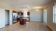 This two-story residence at 8808 North Indian Trail Road in Spokane, Washington offers a well-designed layout with modern finishes throughout. The main level centers around an open-concept kitchen and living area, where light wood-tone flooring flows seamlessly underfoot. The kitchen is outfitted with rich dark wood cabinetry, granite countertops, a tile backsplash, and a full suite of stainless steel appliances including a gas range, microwave, dishwasher, and refrigerator with ice maker. A central island provides additional prep space and casual seating. Pendant lighting and a chandelier add warmth to the space. The adjacent living area is bright and spacious, featuring a ceiling fan, large windows, and a sliding glass door that opens to a private balcony with views of the surrounding neighborhood. A half bathroom with granite vanity and wood-look flooring is also found on the main level. Upstairs, carpeted bedrooms are accessible via a staircase, with an open loft-style landing offering additional views and natural light. A full bathroom features a granite vanity with dark wood cabinetry and a tub-shower combination. The residence also includes a coat closet near the entry and dedicated laundry cabinetry.