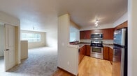 This single-floor residence offers a thoughtfully designed layout that balances functionality and comfort throughout its interconnected spaces. The kitchen is a standout feature, equipped with stainless steel appliances—including a range, microwave, and refrigerator—complemented by warm medium-toned wood cabinetry and granite-style countertops. Track lighting illuminates the space, and light hardwood flooring adds a clean, polished finish. A partial wall separates the kitchen from the adjoining living area, which transitions to plush carpeting and features a built-in electric fireplace, lending a cozy focal point to the room. Natural light filters in through windows fitted with horizontal blinds, offering views of the surrounding exterior.

The bedrooms are carpeted and quietly appointed, each with access to closet storage. One room includes a walk-in closet outfitted with wire shelving and hanging rods, while another features a standard reach-in closet. The primary bathroom offers a wide vanity with dual sinks set into a granite-style countertop, paired with warm wood cabinetry below. A second bathroom provides a single-sink vanity with a matching countertop finish. Textured ceilings are consistent throughout, contributing to the residence's cohesive character.