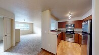 This single-floor residence offers a thoughtfully designed layout that balances functionality and comfort throughout its interconnected spaces. The kitchen is a standout feature, equipped with stainless steel appliances—including a range, microwave, and refrigerator—complemented by warm medium-toned wood cabinetry and granite-style countertops. Track lighting illuminates the space, and light hardwood flooring adds a clean, polished finish. A partial wall separates the kitchen from the adjoining living area, which transitions to plush carpeting and features a built-in electric fireplace, lending a cozy focal point to the room. Natural light filters in through windows fitted with horizontal blinds, offering views of the surrounding exterior.

The bedrooms are carpeted and quietly appointed, each with access to closet storage. One room includes a walk-in closet outfitted with wire shelving and hanging rods, while another features a standard reach-in closet. The primary bathroom offers a wide vanity with dual sinks set into a granite-style countertop, paired with warm wood cabinetry below. A second bathroom provides a single-sink vanity with a matching countertop finish. Textured ceilings are consistent throughout, contributing to the residence's cohesive character.