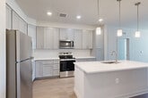 Located at 138 Rosewick Corner Pl in La Plata, MD, this thoughtfully designed 2-bedroom, 2-bathroom residence offers a clean, modern aesthetic throughout its single-floor layout. The open-concept living, dining, and kitchen area serves as the heart of the home, finished with light hardwood-style flooring that flows seamlessly from room to room. The kitchen is a standout feature, showcasing gray shaker-style cabinetry, crisp white quartz countertops, a large center island with an undermount sink, stainless steel appliances including a range, microwave, and refrigerator, and elegant pendant lighting overhead. Recessed lighting and neutral wall tones keep the space bright and inviting. The living area benefits from natural light through a wide window and is equipped with a ceiling fan for added comfort. Both bedrooms are well-proportioned, featuring light flooring, large windows with outdoor views, and ample closet space — including walk-in closets with wire shelving systems. The bathrooms are finished in a clean, contemporary style, with one featuring a tiled tub-surround with subway tiles and a gray vanity. A dedicated in-unit laundry room with full-size washer and dryer adds everyday convenience, completing this well-appointed residence.
