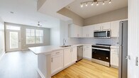 Located at 1000 Fanfare Way in Alpharetta, GA, this single-floor residence offers a clean, modern aesthetic throughout. The open-concept kitchen is a standout feature, showcasing white shaker cabinetry, a classic white subway tile backsplash, quartz countertops, and a peninsula island with an undermount sink. Stainless steel appliances — including a range, microwave, dishwasher, and refrigerator — complete the well-equipped cooking space. Track lighting overhead enhances visibility and adds a contemporary touch. Warm hardwood-style flooring flows through the main living areas, complementing the neutral warm-gray wall tones that create a cohesive, inviting atmosphere. The living area benefits from ample natural light courtesy of large windows with blinds, and is finished with a ceiling fan. A glass-paneled entry door with a transom window above allows additional light into the entryway. Carpeted bedrooms offer comfort and quiet, with generous windows overlooking greenery outside. The primary bathroom includes a white vanity with quartz countertop and direct access to a walk-in closet with wire shelving. Additional utility space with carpeting rounds out the functional layout of this well-designed Alpharetta residence.