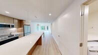 Located at 44 Springside Ave in Poughkeepsie, NY, this thoughtfully designed two-bedroom, one-bathroom residence offers a clean, modern aesthetic throughout its single-floor layout. Light-toned hardwood flooring flows seamlessly across every room, anchoring the bright and airy atmosphere created by crisp white walls and recessed lighting.

The open-concept kitchen serves as a central hub, showcasing warm wood cabinetry, a large white quartz island with pendant lighting, a textured tile backsplash, and a full suite of stainless steel appliances including a dishwasher, range, and over-the-range microwave. The kitchen transitions naturally into a spacious living area bathed in natural light from floor-to-ceiling windows that frame lush outdoor greenery.

The generously sized primary bedroom offers serene views of the surrounding neighborhood through large windows, while the second bedroom provides a clean, versatile space with the same consistent finishes. The full bathroom features a walk-in glass-enclosed shower with tile surround, a floating wood vanity, open wood shelving, and neutral stone-look tile flooring. A dedicated in-unit laundry area houses a full-size Samsung washer and dryer beneath a quartz folding shelf, adding everyday convenience to this well-appointed home.