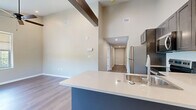 Located at 57 Peak Hill Dr in Rochester, NY, this single-floor, 3-bedroom, 2-bathroom home offers a well-designed layout with modern finishes throughout. The open-concept living and dining area flows seamlessly into a contemporary kitchen featuring stainless steel appliances, dark shaker-style cabinetry, white quartz countertops, a peninsula with an integrated sink, and striking soaring ceilings with a decorative wood beam overhead. Rich hardwood-style flooring runs through the main living spaces, adding warmth and cohesion to the design. The bedrooms are carpeted and receive natural light through large windows that overlook lush greenery, creating a calm and comfortable atmosphere. The spacious primary bedroom includes walk-in closet space with built-in wire shelving. The bathrooms are well-appointed, with one featuring elegant linear-patterned tile flooring, a glass-enclosed shower, a vanity, and an abundance of natural light from large windows. Additional conveniences include dedicated laundry facilities, multiple hallways connecting the rooms efficiently, and ample closet storage throughout. The neutral color palette of warm beiges and soft grays lends a clean, inviting ambiance to every room in this thoughtfully designed home.