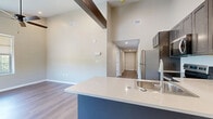 Located at 57 Peak Hill Dr in Rochester, NY, this single-floor, 3-bedroom, 2-bathroom home offers a well-designed layout with modern finishes throughout. The open-concept living and dining area flows seamlessly into a contemporary kitchen featuring stainless steel appliances, dark shaker-style cabinetry, white quartz countertops, a peninsula with an integrated sink, and striking soaring ceilings with a decorative wood beam overhead. Rich hardwood-style flooring runs through the main living spaces, adding warmth and cohesion to the design. The bedrooms are carpeted and receive natural light through large windows that overlook lush greenery, creating a calm and comfortable atmosphere. The spacious primary bedroom includes walk-in closet space with built-in wire shelving. The bathrooms are well-appointed, with one featuring elegant linear-patterned tile flooring, a glass-enclosed shower, a vanity, and an abundance of natural light from large windows. Additional conveniences include dedicated laundry facilities, multiple hallways connecting the rooms efficiently, and ample closet storage throughout. The neutral color palette of warm beiges and soft grays lends a clean, inviting ambiance to every room in this thoughtfully designed home.