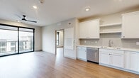 This well-designed one-bedroom, one-bathroom unit in Ankeny, Iowa offers a clean, modern aesthetic with thoughtful use of space throughout. The open-concept kitchen and living area serves as the heart of the home, featuring warm wood-tone luxury vinyl plank flooring, recessed lighting, and a neutral color palette that creates a bright, welcoming atmosphere. The kitchen is outfitted with white shaker-style cabinetry, open shelving, a light gray subway tile backsplash, white countertops, and a full suite of stainless steel appliances including a refrigerator, range, microwave, and dishwasher. A sliding glass door in the living area leads directly to a private balcony, providing outdoor access and views of the surrounding community. The bedroom is a comfortable, well-proportioned room featuring a large black-framed window that fills the space with natural light and an exterior view. A dedicated closet offers convenient storage. The bathroom is finished with white cabinetry, a clean countertop, and a streamlined design. An in-unit stacked washer and dryer are conveniently located in a separate laundry area. Throughout the unit, consistent flooring, clean trim work, and modern hardware contribute to a cohesive, contemporary feel.