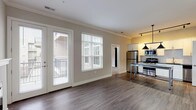 Located at 1221 E Broadway in Louisville, KY, this single-floor residence offers a thoughtfully designed layout with contemporary finishes throughout. The open-concept living area features rich hardwood-style flooring, crown molding, and a sleek fireplace flanked by French doors that open to a balcony, allowing abundant natural light to fill the space. Large windows with blinds further enhance the bright and airy atmosphere.

The kitchen is well-appointed with white shaker cabinetry, a subway tile backsplash, dark stone countertops, stainless steel appliances, and a generously sized island with pendant lighting — ideal for both cooking and casual dining.

The bedroom is carpeted for comfort and showcases a distinctive dark wood sliding barn door, adding a stylish rustic touch. It is complemented by a spacious walk-in closet outfitted with multi-tiered wire shelving for ample storage. A second walk-in closet with hardwood-style flooring provides additional organization space.

Two bathrooms serve the unit: one features a marble-surround walk-in shower, dark stone countertops, and white cabinetry, while the second includes a soaking tub, a large vanity mirror, and matching finishes. A dedicated utility room houses a stacked washer and dryer alongside a water heater, offering convenient in-unit laundry. The overall aesthetic balances modern design with warm, livable details.
