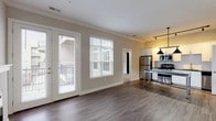 Located at 1221 E Broadway in Louisville, KY, this single-floor residence offers a thoughtfully designed layout with contemporary finishes throughout. The open-concept living area features rich hardwood-style flooring, crown molding, and a sleek fireplace flanked by French doors that open to a balcony, allowing abundant natural light to fill the space. Large windows with blinds further enhance the bright and airy atmosphere.

The kitchen is well-appointed with white shaker cabinetry, a subway tile backsplash, dark stone countertops, stainless steel appliances, and a generously sized island with pendant lighting — ideal for both cooking and casual dining.

The bedroom is carpeted for comfort and showcases a distinctive dark wood sliding barn door, adding a stylish rustic touch. It is complemented by a spacious walk-in closet outfitted with multi-tiered wire shelving for ample storage. A second walk-in closet with hardwood-style flooring provides additional organization space.

Two bathrooms serve the unit: one features a marble-surround walk-in shower, dark stone countertops, and white cabinetry, while the second includes a soaking tub, a large vanity mirror, and matching finishes. A dedicated utility room houses a stacked washer and dryer alongside a water heater, offering convenient in-unit laundry. The overall aesthetic balances modern design with warm, livable details.