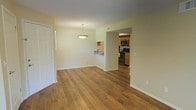 This single-floor residence offers a clean, functional layout with a warm and inviting ambiance throughout. The main living area is highlighted by rich hardwood flooring that extends seamlessly across the space, complementing the neutral, light-toned walls that create a bright and airy atmosphere. A stylish pendant light fixture hangs centrally in the living area, adding a subtle decorative touch while providing focused illumination. A pass-through counter connects the living space to the kitchen area, offering both convenience and an open feel. The kitchen is well-appointed with warm wood cabinetry, a black electric range, and a built-in microwave, providing all the essentials for everyday cooking. The hardwood flooring continues into the kitchen, maintaining a cohesive aesthetic throughout. The layout flows naturally between spaces, making the home feel connected and easy to navigate. Clean white trim and baseboards frame the rooms, adding a crisp finishing detail. The overall design balances practicality with comfort, making it a welcoming and functional living environment.