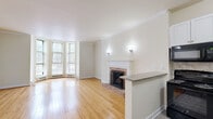 Located at 1518 Park Ave in Baltimore's vibrant Park Avenue corridor, this two-floor residence offers 1 bedroom and 2 bathrooms across a well-appointed layout. The main floor opens into a combined kitchen and living area highlighted by warm hardwood floors, crown molding, and a classic brick fireplace with a white painted mantel. A granite-topped breakfast bar connects the living space to the kitchen, which is outfitted with white shaker cabinets, granite countertops, a tile backsplash, and black appliances including a range, built-in microwave, dishwasher, and refrigerator. Bay windows on the main level flood the space with natural light. A striking wood spiral staircase leads to the upper floor, where the spacious primary bedroom features its own bay window configuration, hardwood flooring, and generous closet storage. The space includes three closets in total. Both bathrooms are tastefully finished — one with large-format tile, a soaking tub/shower combo, and a dark wood vanity, and the other with a dark vanity and brushed nickel fixtures. Neutral tones, crown molding, and classic architectural details throughout lend the space a timeless, refined character.