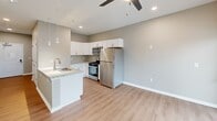 Located at 2635 N Forest Rd in Getzville, NY, this efficiently designed single-floor unit offers a well-appointed layout comprising a kitchen and a full bathroom. The open-concept kitchen serves as the heart of the space, showcasing granite countertops with a double undermount sink, crisp white shaker-style cabinetry, and a full suite of stainless steel appliances including a gas range, built-in microwave, and refrigerator. Stylish pendant lighting illuminates the kitchen peninsula, complementing the recessed ceiling lights throughout. The living area flows naturally from the kitchen, featuring warm-toned luxury vinyl plank flooring, neutral gray walls, and a ceiling fan with integrated lighting. A sliding glass door opens to a private balcony, allowing natural light to fill the space and providing outdoor views. A double closet in the hallway offers practical storage. The bathroom is fitted with a full-size tub and shower surround in a clean, white finish. The overall aesthetic is modern and move-in ready, with consistent finishes and a bright, airy ambiance throughout the unit.
