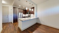 Located at 2949 Parkwood Blvd in Frisco, TX, this one-bedroom, two-bathroom residence offers a well-designed single-floor layout that maximizes functionality and style. The open-concept living, dining, and kitchen area forms the heart of the home, showcasing rich dark-stained cabinetry, granite countertops, a peninsula island with pendant lighting above, and a full suite of stainless steel appliances including a refrigerator, range, microwave, and dishwasher. A white subway tile backsplash and warm hardwood-style flooring complete the kitchen's polished look. The living area benefits from natural light through a large window and a ceiling fan, with access to a private patio. The spacious primary bedroom features plush carpet, a ceiling fan, and generous natural light from wide windows with blinds. It connects to a well-appointed bathroom with dark cabinetry, granite vanity, a soaking tub with tiled surround, and hardwood-style flooring. Abundant storage is provided through five closets, including a large walk-in closet with built-in shelving and hanging rods. A second full bathroom, in-unit laundry, and a welcoming entryway round out this thoughtfully designed residence.
