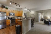 This single-floor residence in Macon, Georgia offers a thoughtfully designed layout that balances functionality and comfort throughout its interconnected spaces. The kitchen is a standout feature, equipped with stainless steel appliances—including an electric range, over-the-range microwave, and dishwasher—complemented by warm honey-toned cabinetry, granite-style countertops, and hardwood flooring. Track lighting illuminates the space, which flows seamlessly into a dining area and an open corridor. A peninsula with bar seating provides a convenient transition point between the kitchen and the adjoining living areas.

The living room features plush carpeting, crown molding, and textured walls with a warm neutral finish. French doors allow natural light to filter in while offering outdoor access. The bedrooms are carpeted and generously sized; the primary bedroom includes a large window with outdoor views and a distinctive wood-paneled accent wall. Both bathrooms are finished with tile flooring, warm wood vanities, granite-style countertops, and tub-shower combinations. One bathroom also includes a walk-in closet. Crown molding appears consistently throughout, lending a polished, cohesive character to the entire residence.