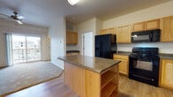Located at 8200 W 20th St in Greeley, Colorado, this single-floor residence offers a well-designed layout that balances functionality and comfort. The kitchen serves as the heart of the home, featuring warm honey-toned oak cabinetry, dark granite-style countertops, and a full suite of black appliances including a side-by-side refrigerator with ice and water dispenser, electric range, over-the-range microwave, and dishwasher. A central island provides additional counter space and open shelving below, making it ideal for meal prep and casual dining. Wood-look flooring flows throughout the kitchen and into the adjacent living area, which is topped with a ceiling fan and opens directly to an outdoor balcony via sliding glass doors, allowing for an abundance of natural light and exterior views. The bedroom features plush carpeting and multiple windows that fill the room with daylight and neighborhood views. The bathrooms are finished with warm terracotta-toned tile flooring, wood-framed vanities with dark countertops, and a full tub-shower combination with built-in shelving. A dedicated entry area with a built-in bench adds a practical touch near the front door, completing this thoughtfully arranged single-level home.