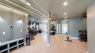 Located at 1911 Saddlebrook Dr in Murfreesboro, Tennessee, this fitness center offers a comprehensively outfitted exercise space across a single floor. The room is designed with a clean, modern aesthetic, featuring soft teal and white walls, light-toned cork-style flooring, and a combination of recessed lighting and linear LED accent strips that illuminate the space with a bright, energetic ambiance. Ceiling fans provide added airflow and comfort throughout the workout area.

The cardio zone is well-stocked with Star Trac treadmills, elliptical machines, and a stationary cycling bike, all positioned in front of large wall-to-wall mirrors that amplify the sense of space. Mounted televisions above the mirrors offer entertainment during workouts. A multi-station cable machine anchors the strength training area, complemented by a dedicated rack housing stability balls in multiple sizes, resistance accessories, and a full dumbbell rack for free weight training. A flat bench and additional functional training equipment round out the strength offerings.

Multiple windows along the exterior walls invite abundant natural light, creating an open, airy feel. The entryway area features a clean, welcoming layout with a sanitation station, a posted fitness center guidelines board, and ample open floor space for stretching or additional exercises. Overall, this fitness center delivers a fully functional and visually appealing environment suited for a wide range of workout routines.