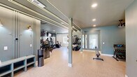 Located at 1911 Saddlebrook Dr in Murfreesboro, Tennessee, this fitness center offers a comprehensively outfitted exercise space across a single floor. The room is designed with a clean, modern aesthetic, featuring soft teal and white walls, light-toned cork-style flooring, and a combination of recessed lighting and linear LED accent strips that illuminate the space with a bright, energetic ambiance. Ceiling fans provide added airflow and comfort throughout the workout area.

The cardio zone is well-stocked with Star Trac treadmills, elliptical machines, and a stationary cycling bike, all positioned in front of large wall-to-wall mirrors that amplify the sense of space. Mounted televisions above the mirrors offer entertainment during workouts. A multi-station cable machine anchors the strength training area, complemented by a dedicated rack housing stability balls in multiple sizes, resistance accessories, and a full dumbbell rack for free weight training. A flat bench and additional functional training equipment round out the strength offerings.

Multiple windows along the exterior walls invite abundant natural light, creating an open, airy feel. The entryway area features a clean, welcoming layout with a sanitation station, a posted fitness center guidelines board, and ample open floor space for stretching or additional exercises. Overall, this fitness center delivers a fully functional and visually appealing environment suited for a wide range of workout routines.