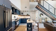 Located in West Los Angeles, this thoughtfully designed two-story home offers one bedroom, two bathrooms, and a dedicated office across two well-proportioned floors. The lower level makes an immediate impression with soaring double-height ceilings, a dramatic floor-to-ceiling mosaic tile accent wall, and polished concrete floors that lend an industrial-modern feel. Large windows flood the living area with natural light, complementing the clean, open layout. A sleek staircase with a black metal mesh railing leads to the upper level, where a warm wood-paneled ceiling creates a cozy yet refined atmosphere. The spacious primary bedroom features the same wood ceiling detail, black-framed windows with views of surrounding greenery, and plush carpeting for comfort. Two well-appointed bathrooms showcase high-end finishes, including gold hardware, floating wood vanities, large-format tile, and a glass-enclosed tub-shower combination. A second bathroom features distinctive hexagonal tile flooring and a vessel sink. The office is bright and functional, with dual windows offering garden views. Throughout the home, a cohesive mid-century modern aesthetic is maintained through warm wood tones, brushed gold accents, and a carefully curated material palette that balances texture and refinement.