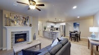 This single-floor home showcases an open-concept layout that effortlessly connects the living, kitchen, and dining areas into one cohesive and functional space. The living room serves as a warm focal point, anchored by a tiled fireplace framed with a classic white mantel, and is complemented by plush carpeting and a ceiling fan with integrated lighting. Recessed lighting throughout ensures the space remains bright and welcoming.

The kitchen is well-appointed with white shaker-style cabinetry, granite-look countertops, and a full suite of stainless steel appliances, including a refrigerator and microwave. A peninsula island with bar seating provides a casual dining option while maintaining the open flow of the space. Pendant lights hang above the island, adding a stylish touch. The kitchen transitions seamlessly into a dedicated dining area, which offers ample room for a full dining set. Light wood-style flooring in the kitchen and dining zone contrasts attractively with the soft carpeting of the living area, creating distinct yet harmonious zones throughout this inviting home.