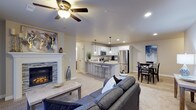 This single-floor home showcases an open-concept layout that effortlessly connects the living, kitchen, and dining areas into one cohesive and functional space. The living room serves as a warm focal point, anchored by a tiled fireplace framed with a classic white mantel, and is complemented by plush carpeting and a ceiling fan with integrated lighting. Recessed lighting throughout ensures the space remains bright and welcoming.

The kitchen is well-appointed with white shaker-style cabinetry, granite-look countertops, and a full suite of stainless steel appliances, including a refrigerator and microwave. A peninsula island with bar seating provides a casual dining option while maintaining the open flow of the space. Pendant lights hang above the island, adding a stylish touch. The kitchen transitions seamlessly into a dedicated dining area, which offers ample room for a full dining set. Light wood-style flooring in the kitchen and dining zone contrasts attractively with the soft carpeting of the living area, creating distinct yet harmonious zones throughout this inviting home.