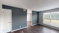 Located at 4216 Garrett Rd in Durham, NC, this single-floor unit presents a clean, contemporary aesthetic throughout. The living area is defined by rich, dark hardwood-style flooring and a cool slate-blue accent wall that adds depth and character to the space. A large window allows natural light to flow in, offering views of the surrounding greenery and creating a welcoming atmosphere. The textured ceiling and crisp white trim complement the neutral color palette used consistently throughout the unit.

The kitchen is well-appointed with white cabinetry, granite-style countertops, a tile backsplash, and a full suite of stainless steel appliances including a refrigerator, electric range, microwave, and dishwasher. Wood-look flooring carries through the kitchen, adding warmth to the functional space.

The bedrooms feature plush gray carpeting and are painted in soft, neutral tones. Each room includes a window fitted with blinds, providing both natural light and privacy. The bathroom is finished with wood-look flooring, a white vanity with an undermount sink, a large mirror, and tile-surround walls, offering a clean and practical design. Overall, the unit provides a well-maintained, move-in-ready living environment with consistent, modern finishes throughout.
