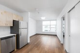 This single-floor unit offers a thoughtfully designed open-concept layout that seamlessly connects the kitchen and living areas, creating a bright and functional living environment. The kitchen is well-appointed with light wood flat-panel cabinetry providing ample upper and lower storage, white countertops, a stainless steel undermount sink, a stainless steel electric range with an overhead ventilation hood, a stainless steel dishwasher, and a full-size refrigerator. The kitchen's L-shaped configuration maximizes workspace and efficiency. Warm hardwood-style flooring flows consistently throughout the main living areas, adding a sense of warmth and continuity to the space. The living area is open and versatile, bathed in natural light from a window, with clean white walls and flush-mount ceiling lighting that keep the atmosphere bright and airy. The bathroom features a full soaking tub with a clean white surround, brushed nickel hardware, and a crisp, minimalist finish. An additional room with hardwood-style flooring and neutral white walls offers flexible use as a bedroom or private space. The unit's clean, contemporary aesthetic and practical layout make it a comfortable and functional living space.