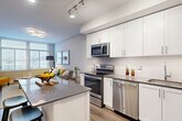 Located at 3400 South Clark Street in Arlington, VA, this well-appointed one-bedroom, one-bathroom residence offers a thoughtfully designed single-floor layout. The open-concept kitchen and dining area serves as the heart of the home, showcasing crisp white shaker cabinetry, a full suite of stainless steel appliances including a range, microwave, and dishwasher, a subway tile backsplash, and a granite-topped island with bar seating — ideal for casual dining and entertaining. Light wood-style flooring runs throughout the main living areas, adding warmth and continuity.

The living room is bright and welcoming, with large windows that invite generous natural light and provide views of the surrounding neighborhood. The bedroom, finished with plush carpeting, features a dedicated window and ample closet space — with four closets distributed throughout the unit providing excellent storage. The full bathroom includes a tiled tub-shower combination and a vanity with a dark stone countertop.

Additional practical features include in-unit laundry, a hallway entry with a distinctive dark wood door, and track lighting throughout the kitchen. The overall aesthetic is clean and modern, with a neutral color palette that creates a calm, cohesive atmosphere throughout the home.