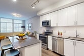 This contemporary 590 square foot apartment in Arlington, VA showcases a thoughtful design that maximizes space and style. The heart of the home is an open-concept kitchen and living area, characterized by clean lines and a neutral color palette. The kitchen boasts crisp white cabinetry, stainless steel appliances, and a functional island with seating, perfect for casual dining or entertaining.

The living room is flooded with natural light from large windows and features hardwood floors, creating a warm and inviting atmosphere. A grey sectional sofa anchors the space, complemented by pops of yellow in the decor, adding a vibrant touch to the room.

The bedroom, measuring 150 square feet, continues the modern aesthetic with a plush bed, wooden dresser, and ample natural light. The bathroom is sleek and efficient, with a white vanity, large mirror, and a shower/tub combination.

Throughout the apartment, clever storage solutions and multi-functional furniture pieces make the most of the compact layout. Track lighting and contemporary fixtures add to the overall modern ambiance. This well-designed space offers a perfect blend of style and functionality for urban living.