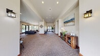 Located in East Wenatchee, WA, this single-story community clubhouse offers a thoughtfully designed gathering space with a welcoming atmosphere throughout. The entrance greets visitors with soaring ceilings, large glass double doors, and an abundance of natural light streaming through oversized windows that frame views of the surrounding outdoor pool area.

The expansive main living area features warm, neutral tones, textured carpeting, and recessed lighting. A tiled fireplace with a wall-mounted TV serves as a focal point, complemented by comfortable leather seating. Adjacent to this lounge area is a functional kitchenette outfitted with wood cabinetry, granite-style countertops, a built-in microwave, and a compact refrigerator — ideal for community events.

A connected hallway leads to a bright, windowed game room equipped with a ping-pong table, bookshelf, and café-style seating, making it a versatile recreational space. Two clean, tile-floored bathrooms serve the facility, one of which is ADA-accessible with grab bars for added convenience.

Throughout the space, large windows and glass doors maintain a strong visual connection to the outdoors, while the open floor plan and high ceilings contribute to an airy, inviting ambiance suitable for a variety of community gatherings.