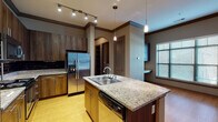 Located in the heart of Tulsa at 10 East Archer Street, this single-floor residence offers a thoughtfully designed layout with contemporary finishes throughout. The open-concept kitchen serves as a central hub, showcasing rich dark wood cabinetry that extends to the ceiling, granite countertops, a large center island with a double-basin sink and pendant lighting, and a full suite of stainless steel appliances including a refrigerator, range, and built-in microwave. A dark subway tile backsplash and hardwood flooring add a polished, modern character to the space. The spacious living area flows naturally from the kitchen, featuring warm hardwood floors, crown molding with decorative trim details, an architectural column, and generous windows that invite abundant natural light. The bedrooms are carpeted for comfort, with large windows offering outdoor views and ceiling fans for added convenience. The bathrooms are finished with light ceramic tile flooring, granite-topped vanities, tall wood cabinetry for ample storage, and tiled shower surrounds. A dedicated laundry area accommodates a full-size washer and dryer side by side. The unit's neutral warm-toned palette, quality finishes, and functional layout come together to create a comfortable and refined urban living environment.