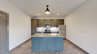 This thoughtfully designed 2-bedroom, 2-bathroom residence is laid out on a single floor, offering a functional and cohesive living experience. Light wood-grain flooring runs throughout the space, tying together each room with a clean, contemporary aesthetic.

The kitchen serves as a central highlight, featuring floor-to-ceiling gray shaker-style cabinetry with brushed nickel hardware, a white hexagonal tile backsplash, and stainless steel appliances including a refrigerator, range, and microwave. A kitchen island with a granite countertop and undermount sink provides additional prep space and casual seating potential. Pendant lighting and recessed fixtures illuminate the area effectively.

The open living area adjoins the kitchen and benefits from natural light via large gridded windows, a ceiling fan, and direct access to an outdoor balcony through a glass-panel door.

The spacious primary bedroom features multiple windows for ample natural light, a ceiling fan, and access to a walk-in closet with built-in shelving. The second bedroom mirrors similar finishes and also enjoys natural light through gridded windows.

Both bathrooms are finished consistently, each offering a gray shaker vanity with granite countertops, a framed mirror, modern light fixtures, floating shelves, and tile flooring. One bathroom includes a soaking tub with tiled surround, while the other features a glass-enclosed shower.
