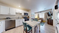 Located at 411 W Maple St in Wichita, Kansas, this well-appointed one-bedroom, one-bathroom unit offers a smart, functional layout across a single floor. Light-toned wood-look flooring runs throughout, lending a clean, cohesive feel to the entire space.

The open-concept kitchen and living area serves as the heart of the unit. The kitchen is outfitted with white shaker-style cabinetry, stainless steel appliances including a refrigerator, electric range, over-the-range microwave, and dishwasher, as well as a double basin sink and ample counter space. A compact dining table with teal accent chairs sits adjacent to the kitchen, providing a dedicated eat-in area. The living room features comfortable seating, a window with natural light, and colorful wall art that adds a welcoming touch.

The bedroom is a calm, restful retreat with a large window allowing natural light to filter through neutral drapes. It includes a king-sized bed, bedside lamps, a dresser, and a wall-mounted television. A stacked washer and dryer unit is conveniently located within the unit, adding practical in-unit laundry access. The bathroom offers a full tub-shower combination with clean white finishes. Overall, the space delivers a comfortable, move-in-ready environment with thoughtful amenities throughout.