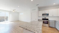 This two-story home is thoughtfully designed across two levels, with the main floor housing the primary living areas and the upper level providing additional private space. The open-concept kitchen and living area anchors the main floor, featuring light hardwood flooring, recessed lighting, and a ceiling fan. The kitchen is outfitted with stainless steel appliances, a built-in microwave, a full-size refrigerator, and a dishwasher. White shaker-style upper cabinets contrast elegantly with soft gray lower cabinets, all complemented by granite countertops and a classic subway tile backsplash. A large granite-topped kitchen island adds additional workspace and seating potential. The living area flows naturally from the kitchen, bathed in natural light from well-placed windows. The three bedrooms offer a mix of hardwood and plush carpet flooring, each with ceiling fans and ample natural light. The primary bedroom includes sliding glass door access and features hardwood floors. Closets provide generous storage with built-in hanging rods. The three bathrooms are finished with granite vanity tops, gray cabinetry, brushed gold fixtures, and wood-look flooring, with at least one featuring a full tub-shower combo. Clean white walls and modern panel doors unify the home's crisp, contemporary aesthetic throughout.