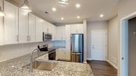 Located at 5840 Farrington Road in Chapel Hill, NC, this well-appointed single-floor residence offers a thoughtfully designed layout with contemporary finishes throughout. The kitchen serves as a central highlight, showcasing crisp white shaker cabinetry, granite countertops, a subway tile backsplash, and a full suite of stainless steel appliances including a range, built-in microwave, and refrigerator. A peninsula with pendant lighting and an undermount sink provides both additional prep space and a natural divide between the kitchen and the open living area. The living area features dark hardwood-style flooring, neutral gray walls, and a ceiling fan, with French doors that open to a private balcony, filling the space with natural light and outdoor views. Bedrooms are finished with plush carpet and generous windows that invite additional natural light. Walk-in closet space with wire shelving systems provides practical storage. The bathroom continues the granite theme with a matching vanity countertop, undermount sink, brushed nickel fixtures, and a large mirror. Clean white trim and neutral tones throughout create a cohesive, modern aesthetic well suited to a variety of lifestyles.