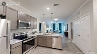 This single-floor residence is thoughtfully designed with an open-concept layout that seamlessly connects the kitchen, dining, and living areas. The kitchen is equipped with stainless steel appliances, including a range, microwave, refrigerator, and dishwasher, complemented by taupe cabinetry, light granite-style countertops, and a peninsula with pendant lighting overhead. Crown molding and light wood-look flooring flow throughout the common areas, enhancing the bright, cohesive aesthetic.

The dining area benefits from abundant natural light through large windows and French doors that open to an outdoor patio, creating an airy connection to the exterior. The primary bedroom features plush carpeting, a ceiling fan, and direct access to a spacious en-suite bathroom with a dual-sink vanity, dark cabinetry, and a large mirror with well-lit sconces. A generously sized walk-in closet with built-in shelving and hanging rods provides ample storage. A second bedroom offers similar comfort with carpet flooring and ceiling fan. A secondary bathroom includes a single vanity, dark cabinetry, and accessibility-friendly grab bars, finished with light wood-look flooring consistent with the rest of the residence.