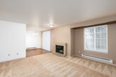 This single-floor residence offers a practical and comfortable layout with a variety of functional spaces thoughtfully connected throughout. The living room serves as the heart of the home, highlighted by a classic brick fireplace set against a warm accent wall, plush carpeting underfoot, and a window with blinds that allows natural light to filter in alongside baseboard heating. An adjacent dining area features an elegant chandelier and opens seamlessly to the kitchen, which is outfitted with white cabinetry, dark laminate countertops, white appliances including a refrigerator, electric range, and microwave, and a peninsula breakfast bar that provides additional prep and seating space. Hardwood-style flooring runs through the kitchen and connecting hallways, adding warmth and continuity to the space. The bedrooms are carpeted and bright, each featuring windows with natural views and baseboard heating. The bathrooms are clean and functional, one featuring a tub-shower combination with hardwood-style flooring, while another includes a full tub-shower with updated chrome fixtures. A dedicated laundry area with a washer and dryer is conveniently located near the bathroom, adding significant utility. The hallway connects all areas efficiently, completing this well-organized and move-in-ready single-floor home.